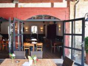 Einladendes Restaurant mit roten Holzelementen und offenen Türen zeigt gemütliche Sitzgelegenheiten innen und außen.