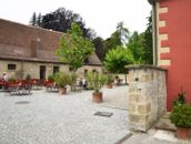 Ein ruhiger Innenhof mit gepflastertem Boden, umgeben von alten Gebäuden und Sitzbereichen mit Tischen und Stühlen.