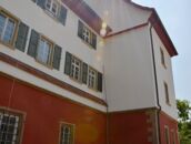 Das rote Schloss erstrahlt im Sonnenlicht, das über die Fassade mit grünen Fensterläden scheint.