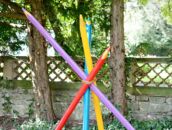 Bunte, riesige Buntstifte sind kreuzweise vor Bäumen auf dem Schlosscampus als Kunstinstallation aufgestellt.