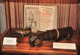 Zwei metallene Prothesenhände und ein altes Buch sind in einer Vitrine mit historischen Beschreibungen ausgestellt.