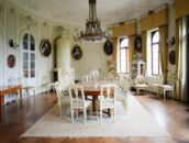 Ein elegantes Esszimmer mit einem großen Holztisch, umgeben von antiken Stühlen und Porträts an den Wänden.