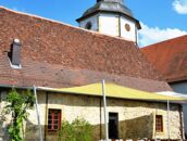 Ein malerischer Schlosshof mit Sitzgelegenheiten und Sonnensegel lädt bei blauem Himmel zum Verweilen ein.