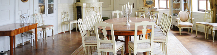 Ein eleganter Speisesaal mit einem großen Holztisch und weißen Stühlen steht bereit für ein formelles Dinner.