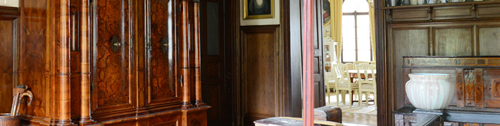 Ein elegantes, hölzernes Interieur mit antikem Schrank und Blick auf einen hellen Essbereich mit weißen Stühlen.